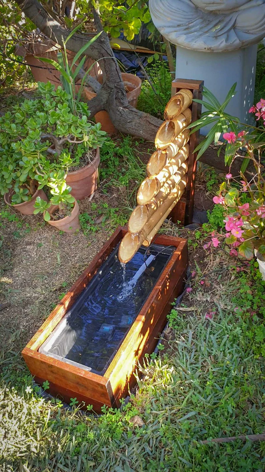 Vue rapprochée de la cascade en bambou alimentant le bassin de la fontaine dans la végétation.